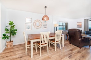 A dining area with a wooden table and chairs, a hanging light fixture, and a view of the ocean through a window. - 501 Sandcastle S. in Ponce Inlet, FL (Ponce Inlet)