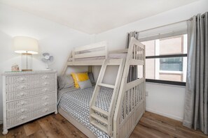 Ein Stockbett mit einer Leiter, ein Nachttisch mit Lampe und eine Kommode mit Schubladen.