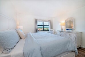 A bedroom with a bed, a dresser, a mirror, and a window with a view. - 501 Sandcastle S. in Ponce Inlet, FL (Ponce Inlet)