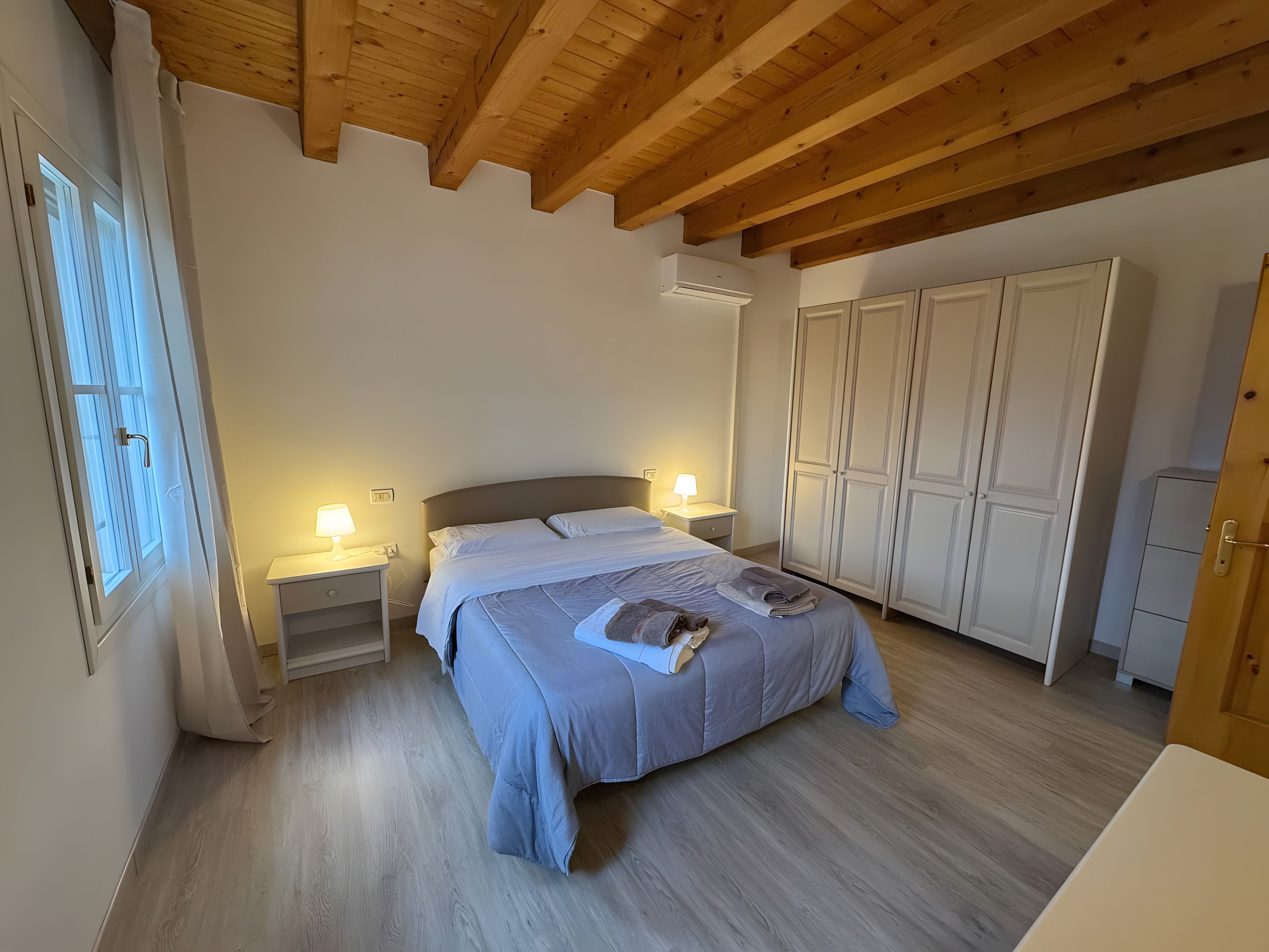 Ein Schlafzimmer mit einem Bett, Nachttischen, einem Kleiderschrank und Holzbalken an der Decke.