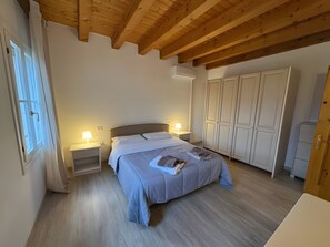 Un dormitorio con cama, mesitas de noche, armario y vigas de techo de madera.