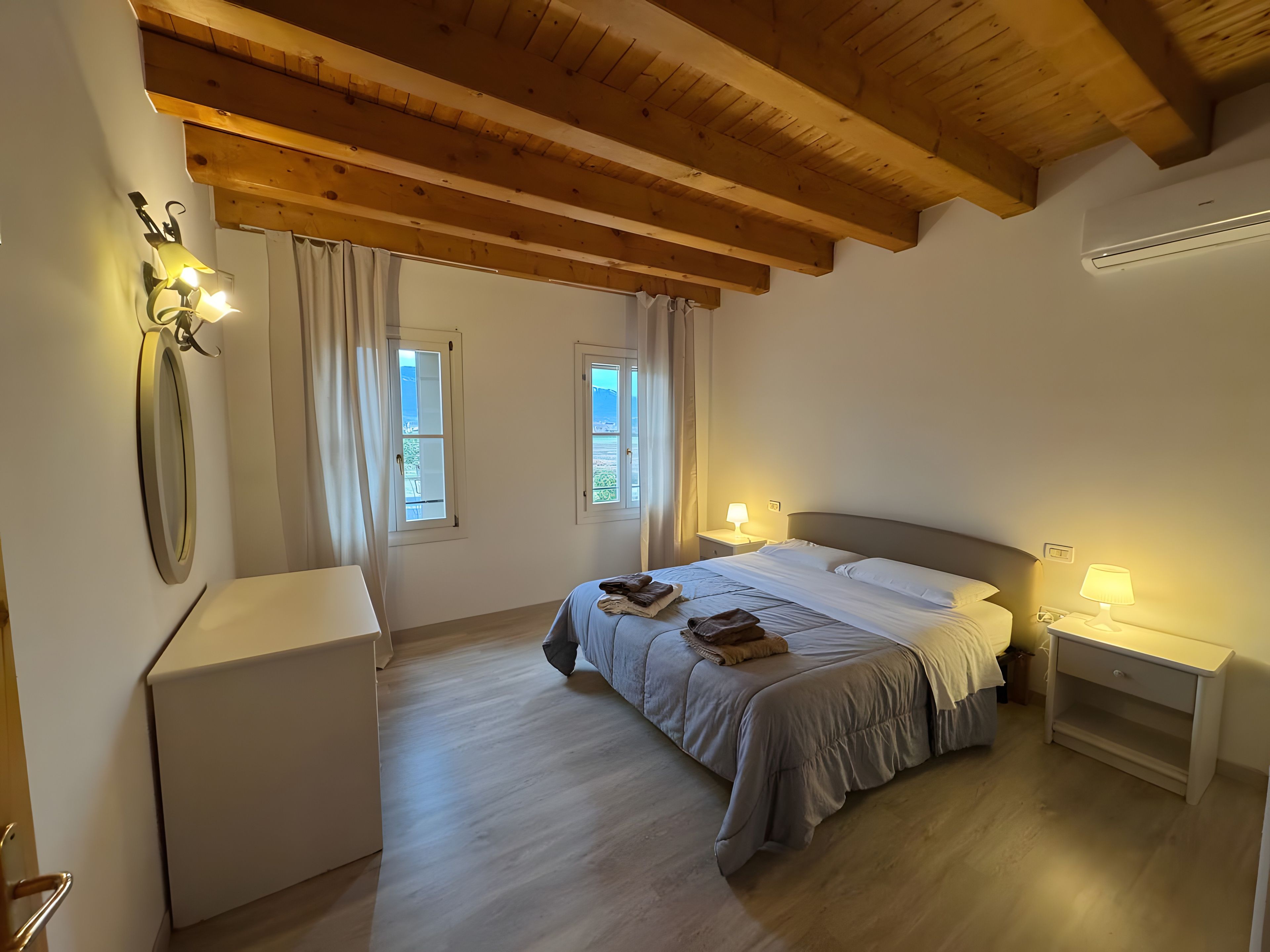 A bedroom with a bed, bedside tables, a mirror, and windows.