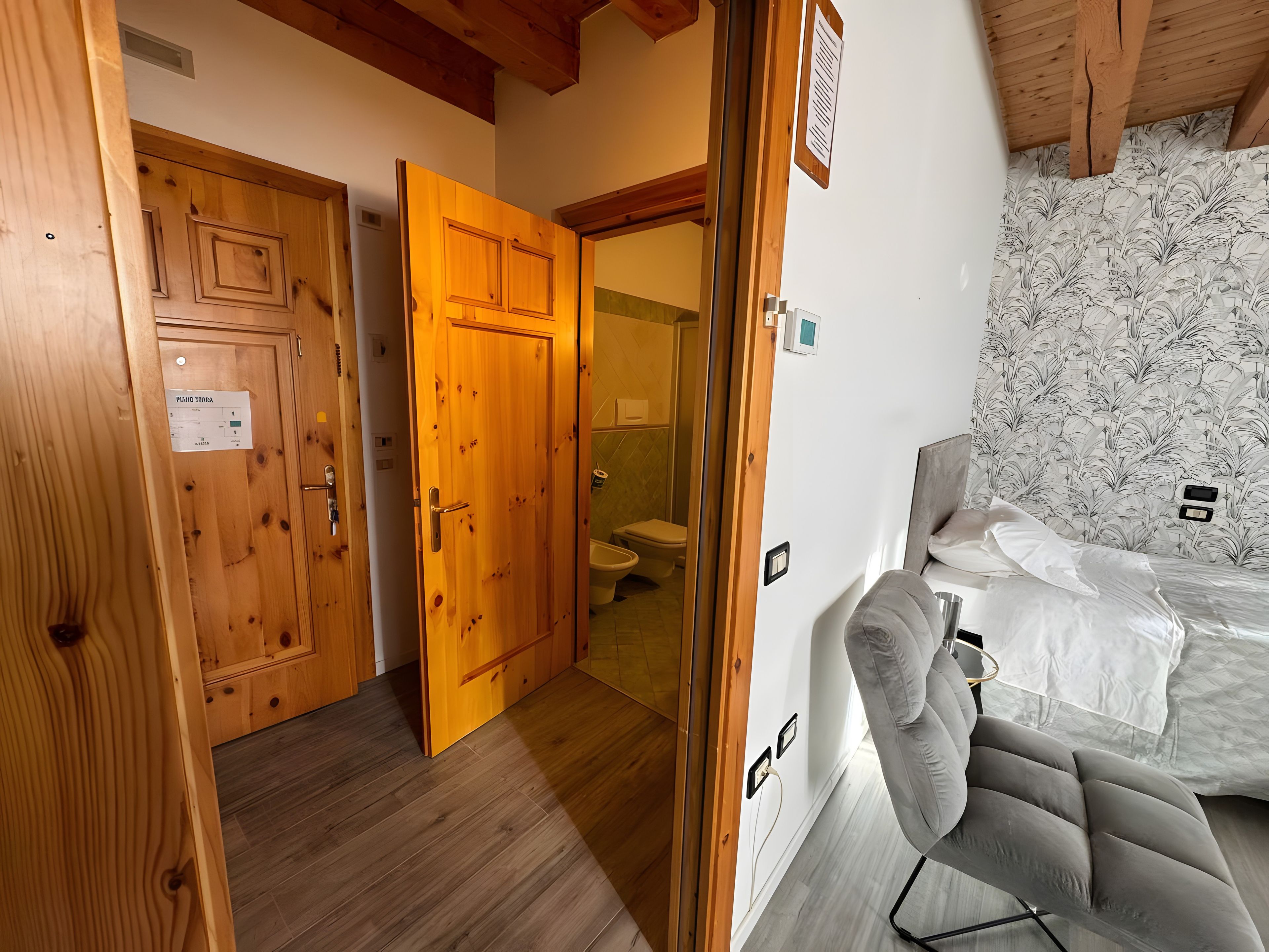 Une pièce avec une porte en bois, un lit avec du linge de lit blanc et une salle de bain avec des toilettes et une douche.