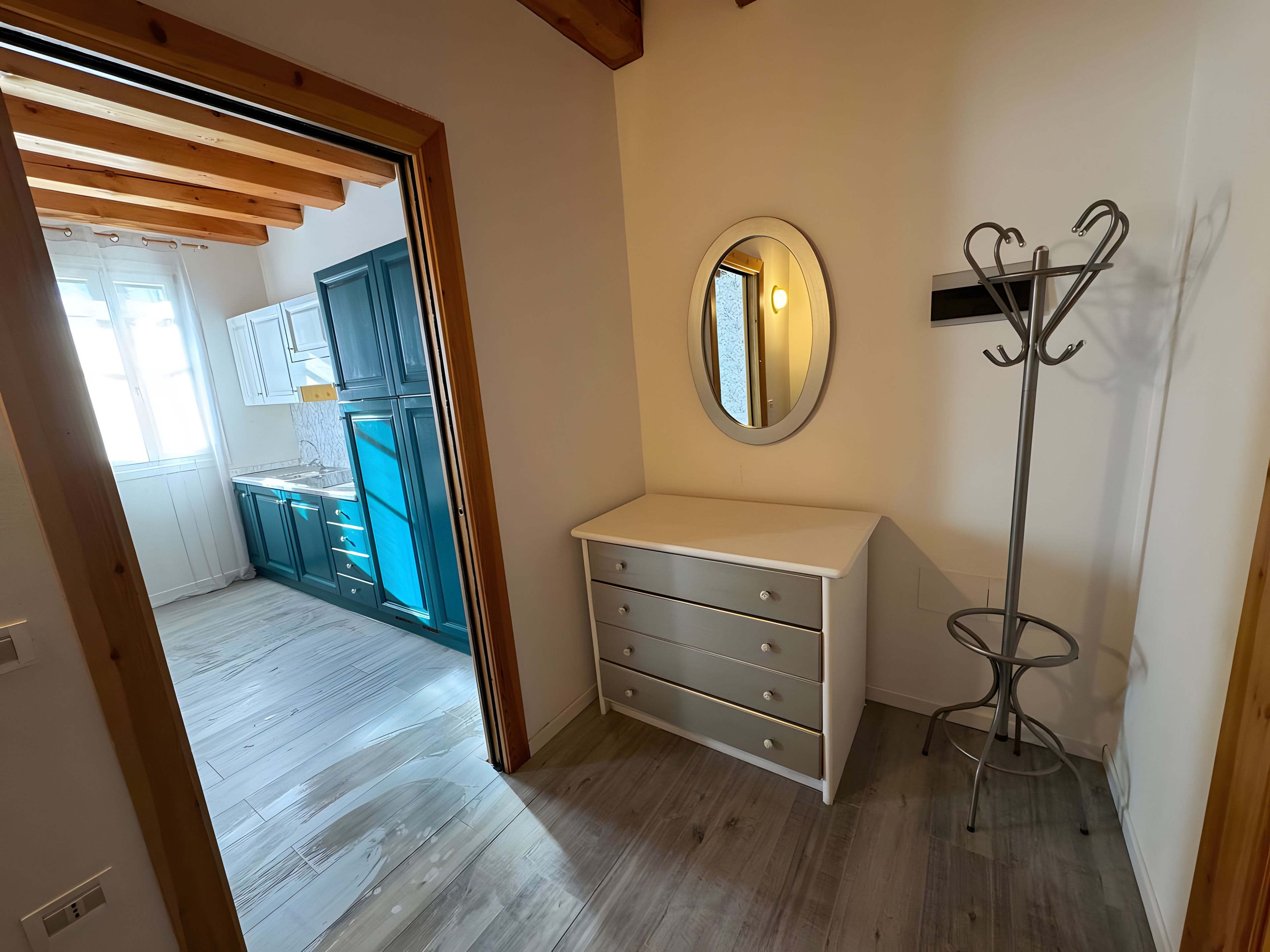 Une pièce avec un plancher en bois, une commode blanche, un miroir et un porte-manteau.