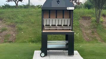 Ein tragbarer Grill mit Schornstein, Rädern und einem Etikett in einer grünen, grasbewachsenen Umgebung.