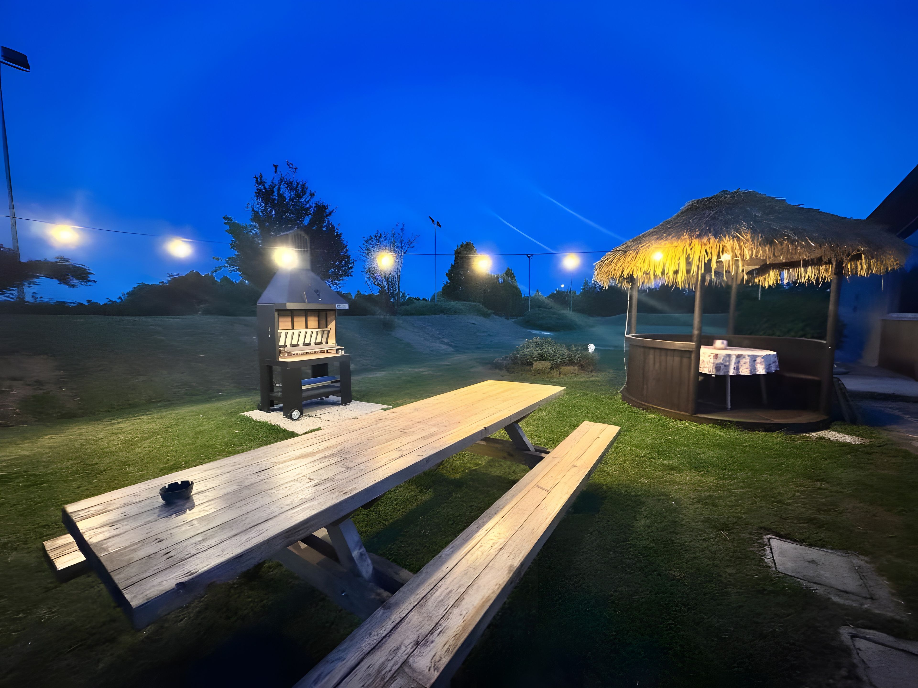 Un espace barbecue extérieur comprenant un gril, une table de pique-nique en bois et un jacuzzi.