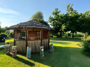 Un belvédère en bois, doté d’un toit de chaume, entouré d’une pelouse bien entretenue et d’arbres.