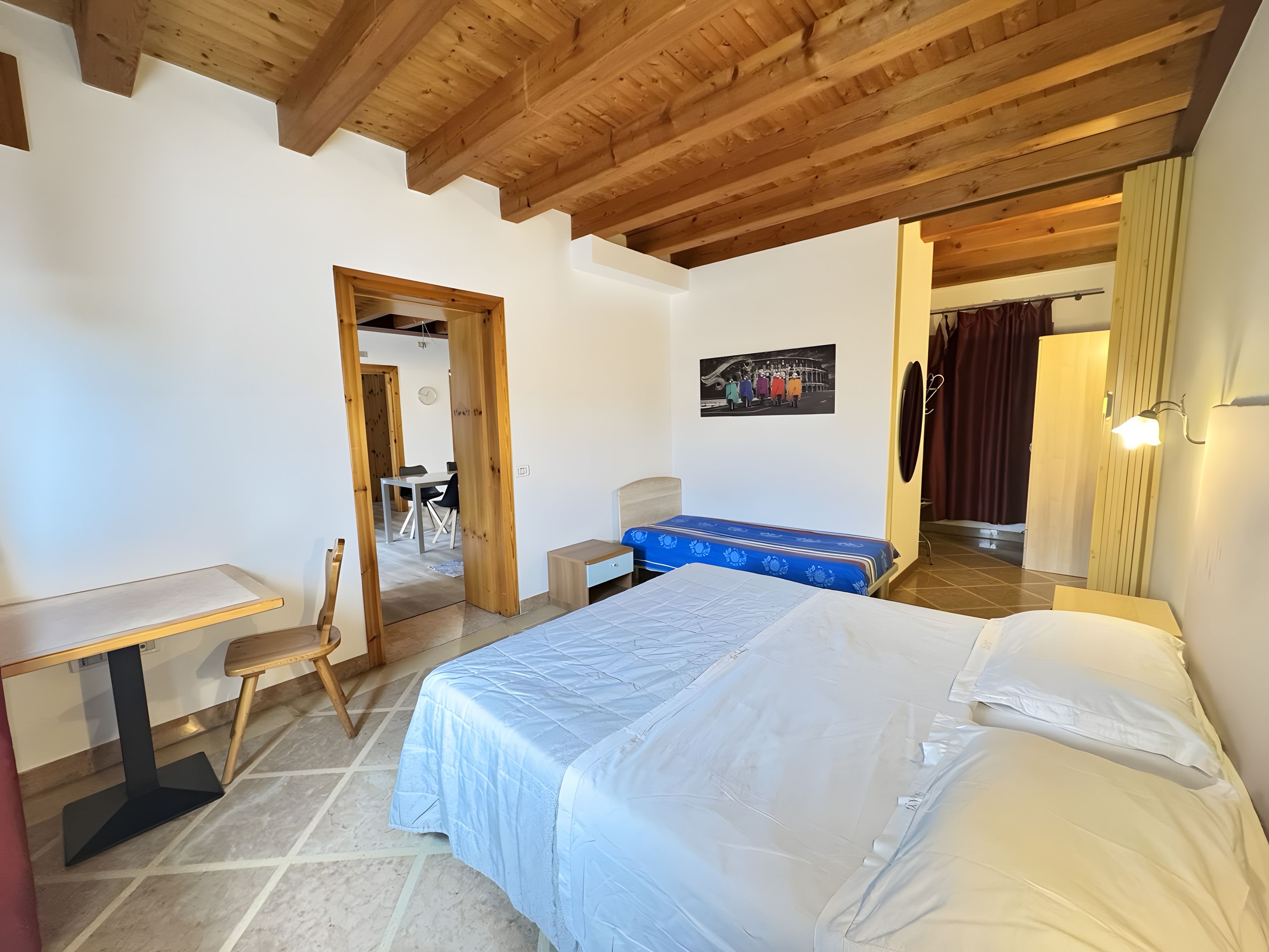 Une chambre à coucher avec un lit, un bureau et une chaise. Une porte donne accès à une autre pièce.