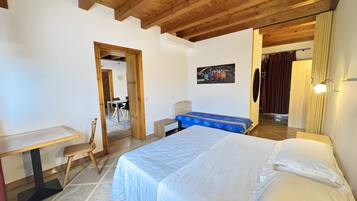 Une chambre à coucher avec un lit, un bureau et une chaise. Une porte donne accès à une autre pièce.