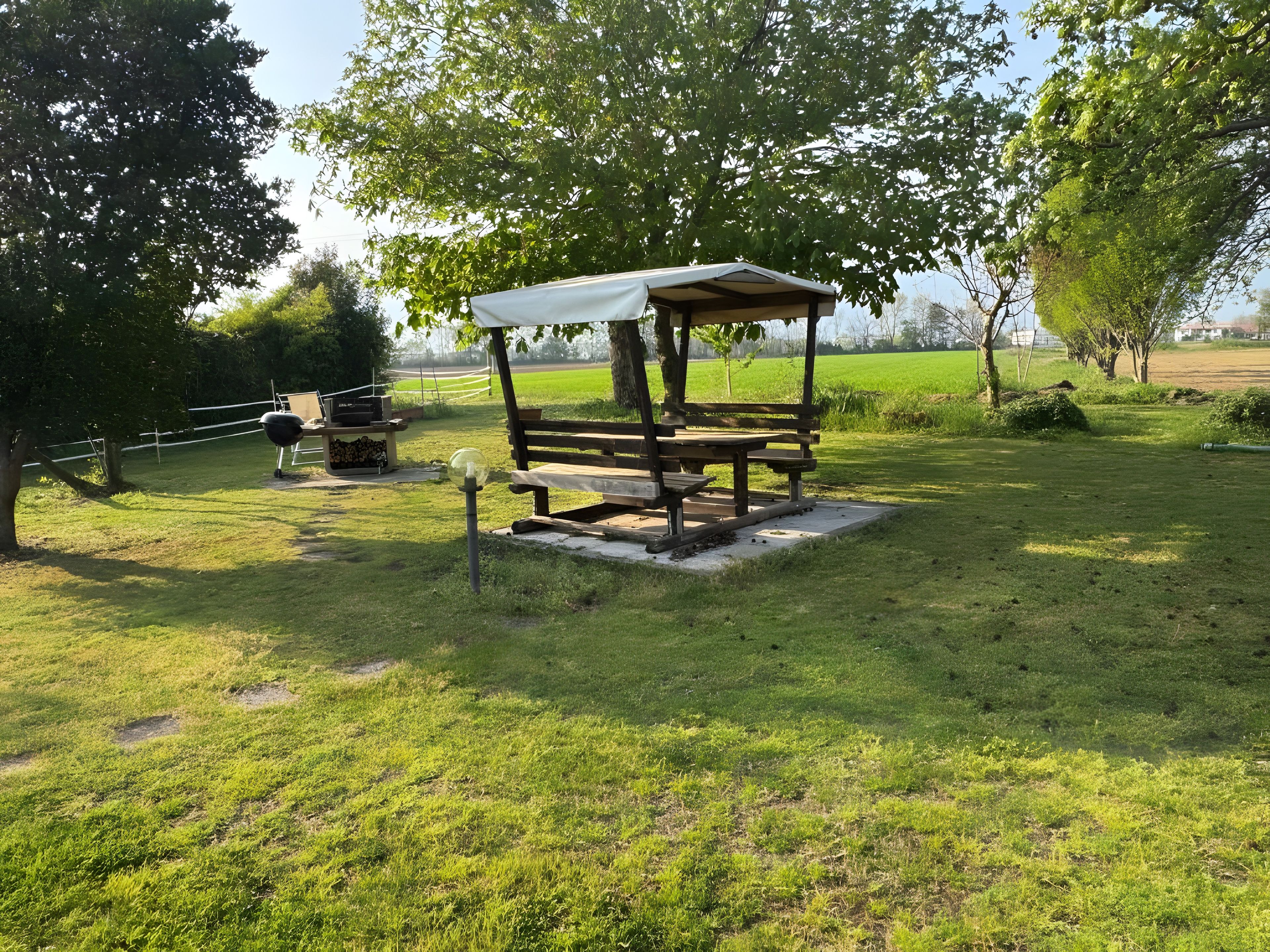 Un espace pique-nique avec un banc et une table en bois, entouré d’herbe et d’arbres.