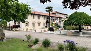 Un edificio con techo de tejas, varias ventanas y un patio empedrado con plantas en macetas y un árbol.