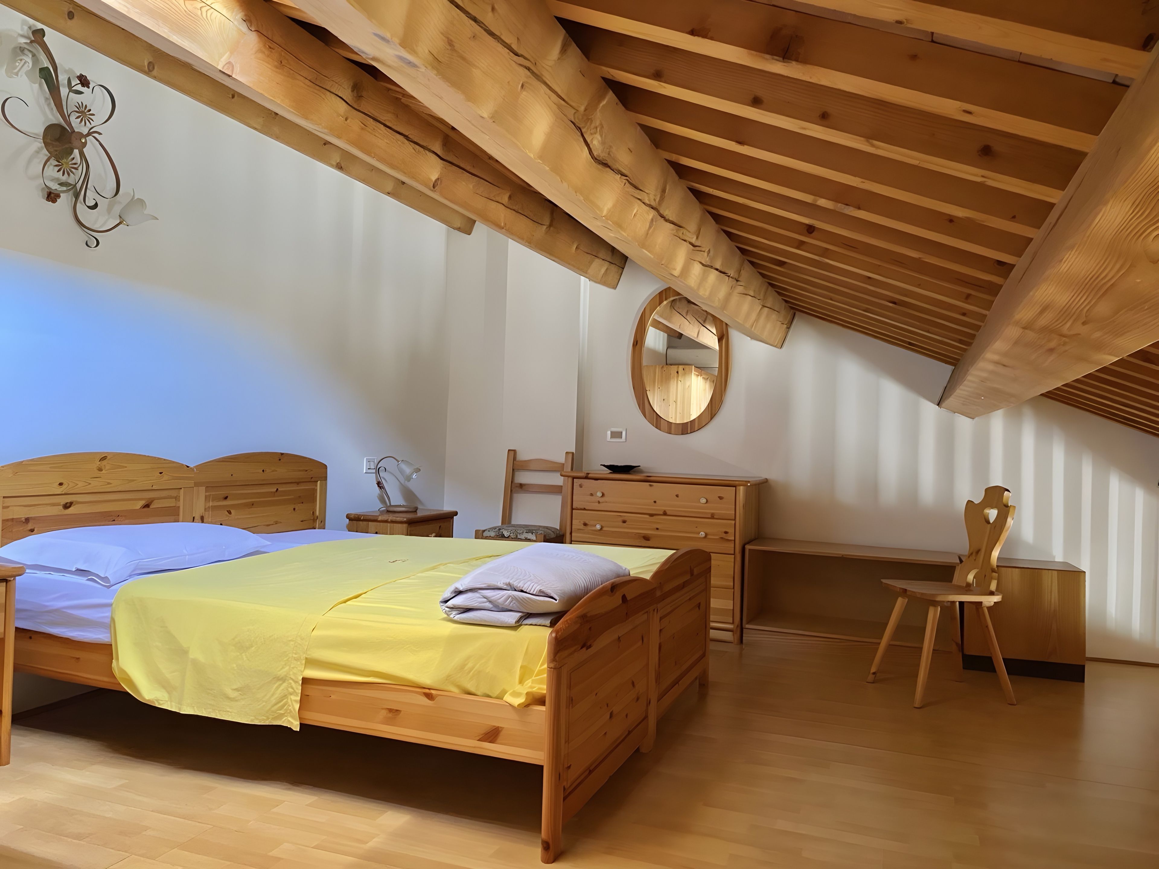 Une chambre à coucher avec un lit en bois, une commode, une chaise, un bureau et un miroir.