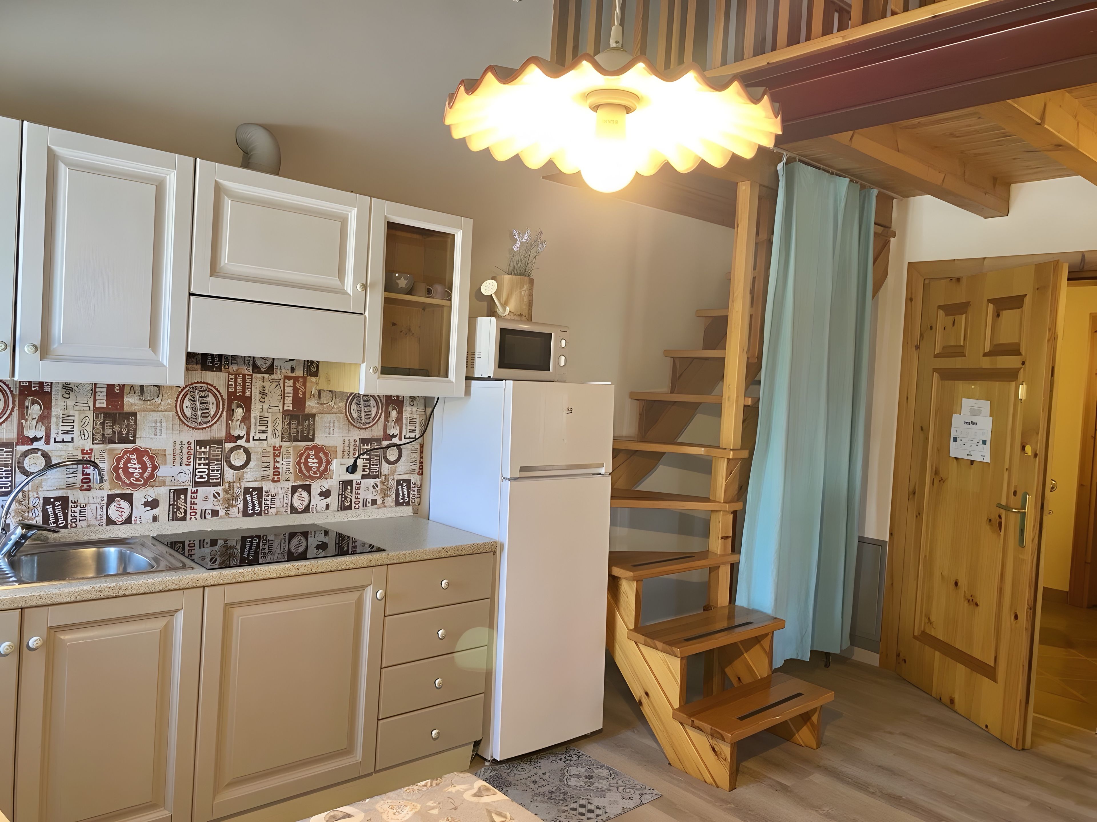 Une cuisine avec des meubles blancs, un four à micro-ondes et un escalier en bois.