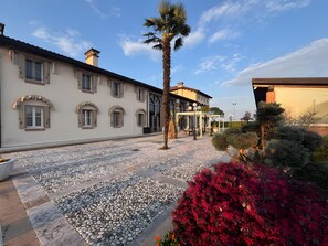 Un edificio con patio piastrellato, una palma e fogliame rosso.