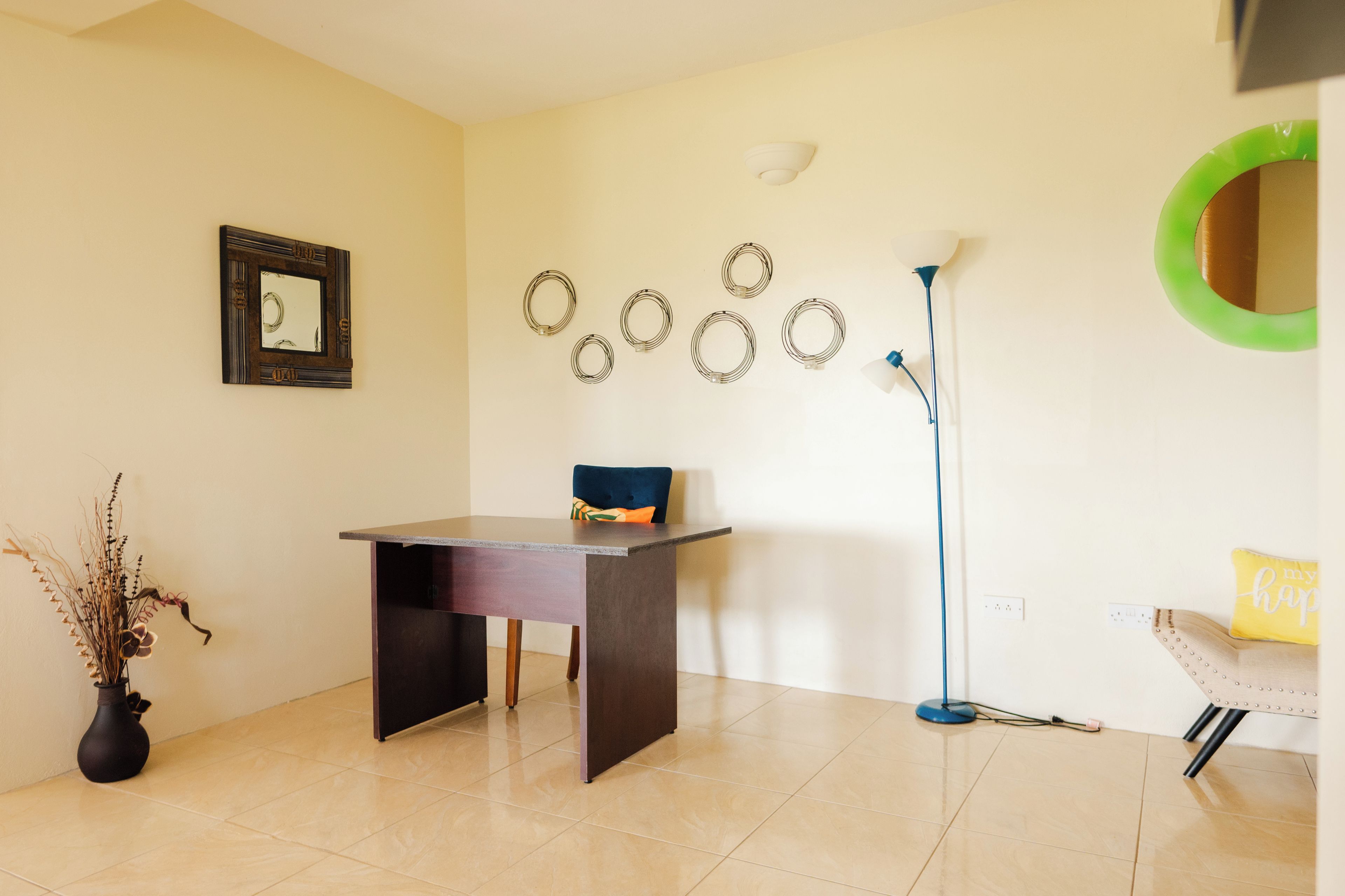 A room with a desk, chair, lamp, wall decorations, and a vase.