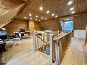 A spacious attic bedroom with a wooden ceiling, a desk with a computer, a chair, and a bed.