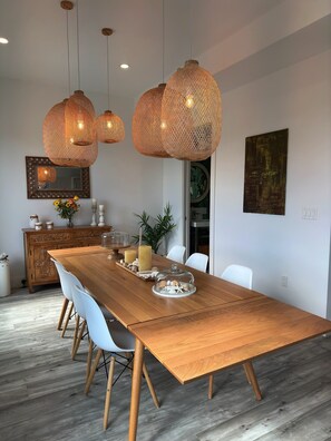Une salle à manger moderne avec une longue table en bois, des chaises blanches et trois grandes suspensions en fibres tressées.