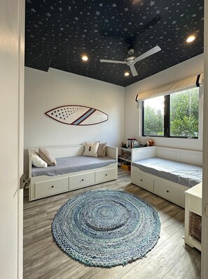 Une pièce avec un motif d’étoiles au plafond, un ventilateur de plafond, un lit doté de tiroirs de rangement, une fenêtre avec vue et une décoration murale représentant une étoile de mer.