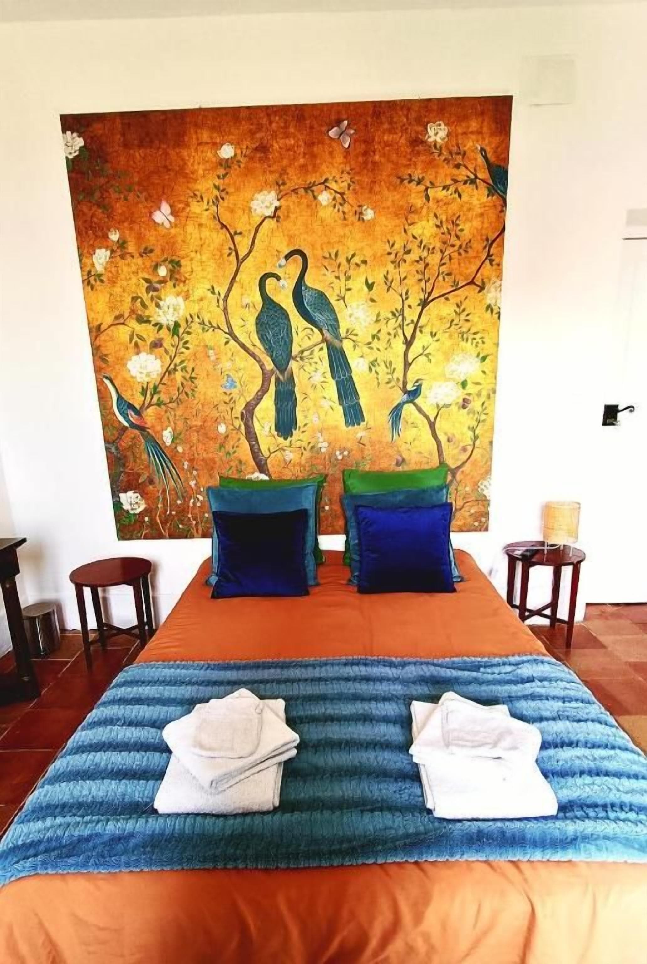 A hotel room with a bed, a painting of birds on the wall, and a blue striped area rug.