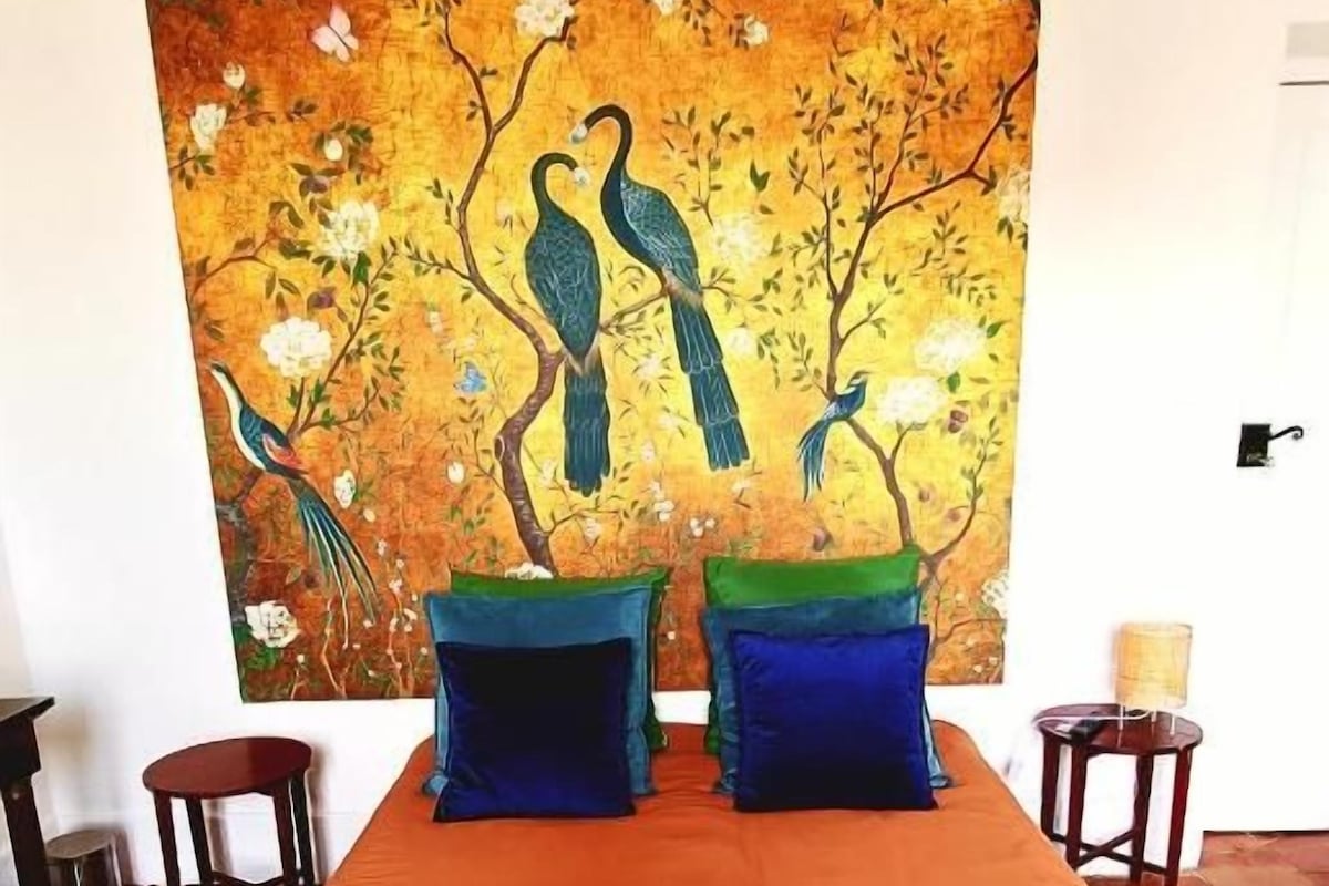 A hotel room with a bed, a painting of birds on the wall, and a blue striped area rug.