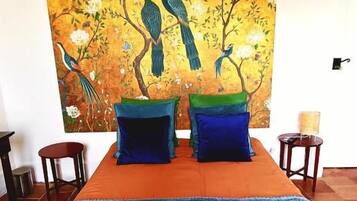 A hotel room with a bed, a painting of birds on the wall, and a blue striped area rug.