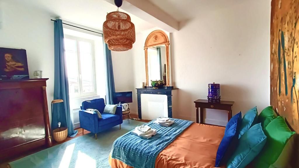 Un dormitorio con una cama, un sillón azul, un aparador, un espejo y una ventana.
