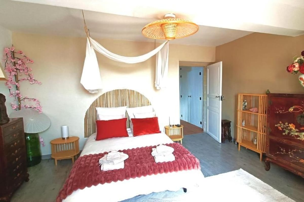 A bedroom with a bed, a bedside table, a lamp, a dresser, and a door leading to another room.