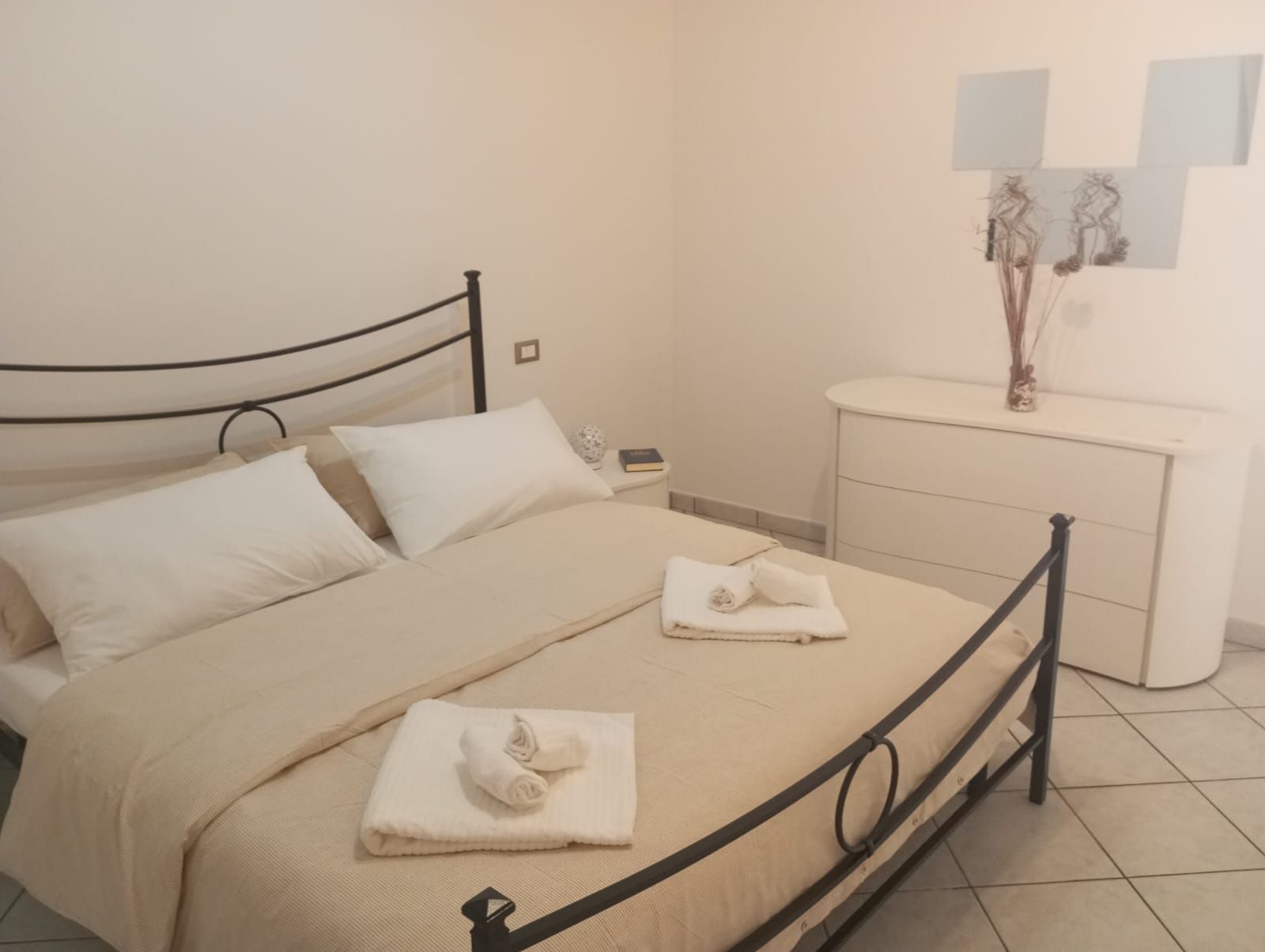 Una cama con estructura metálica, una mesita de noche y un espejo instalado en la pared.