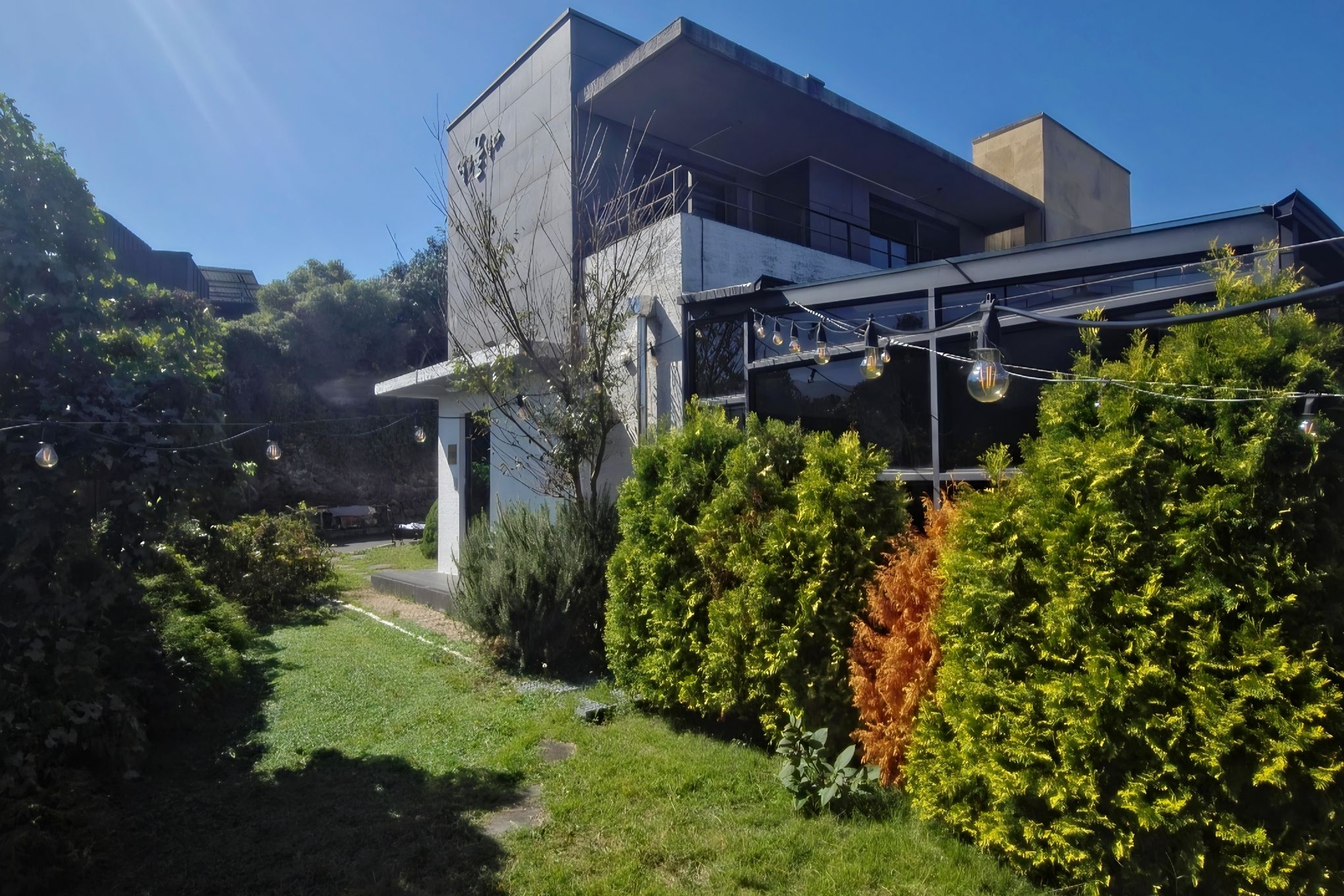 Un bâtiment moderne doté d’un toit plat, d’une entrée bien visible et d’un jardin bien entretenu, agrémenté de divers arbustes et d’un sentier.