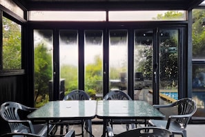 Eine überdachte Terrasse mit Glasveranda, ausgestattet mit Tisch und Stühlen, und Blick auf Grünfläche.