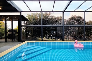 An indoor swimming pool with clear blue tiles, a pink flamingo float, and a view of trees through large windows. - dalkompoolvilla (Jeju-si)