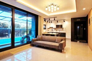 A modern living room with a large window, a sofa, and a kitchen in the background. - dalkompoolvilla (Jeju-si)