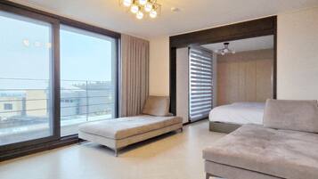 A modern hotel room with a large sliding glass door leading to a balcony, a sofa, a bed, and a ceiling light fixture.