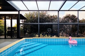 An indoor swimming pool with clear blue tiles, a pink flamingo float, and a view of trees through large windows. - dalkompoolvilla (Jeju-si)