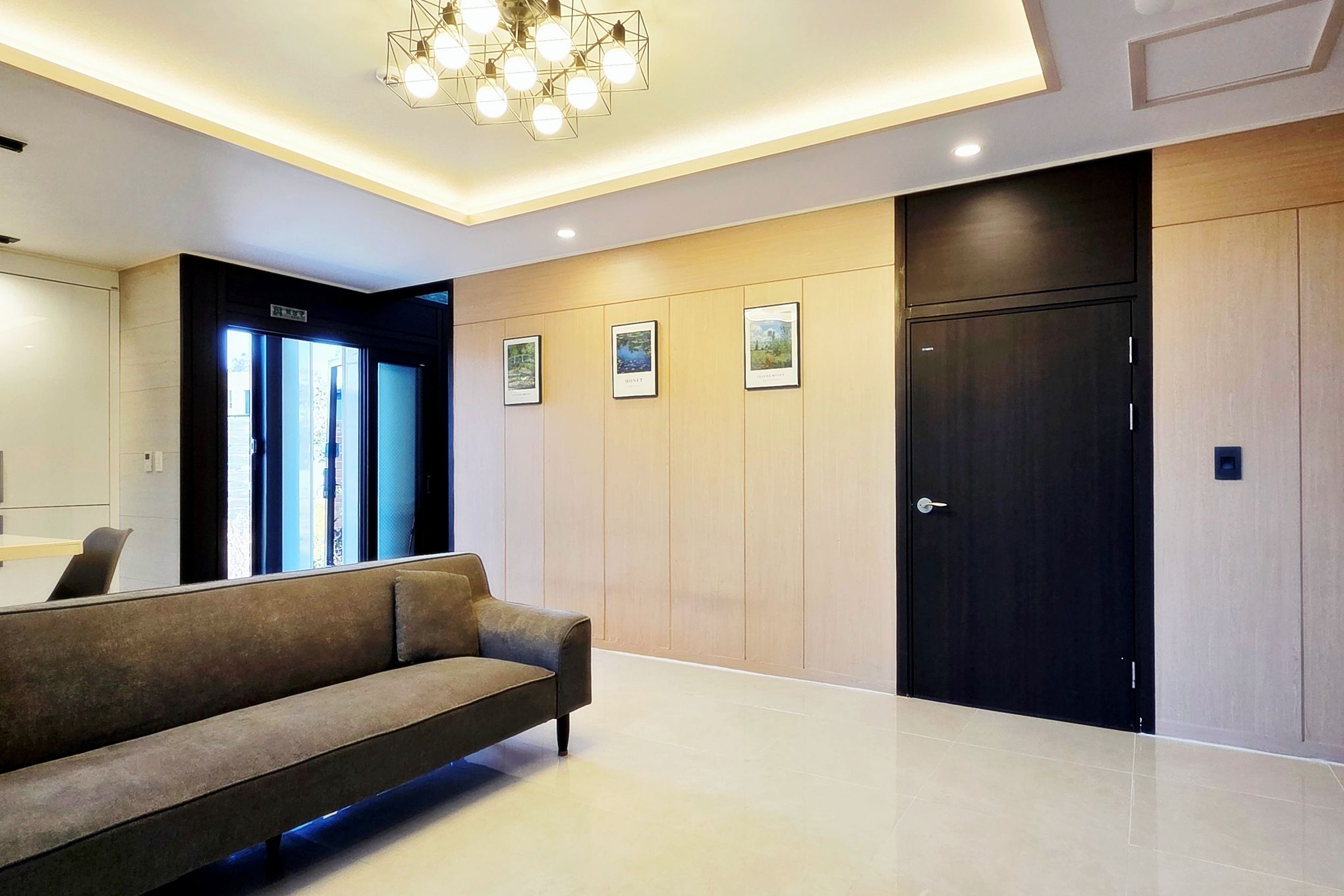 A modern lobby with a sofa, framed pictures, a door, and a ceiling light fixture.