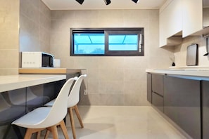 Una cocina moderna con ventana, sillas blancas y un microondas.