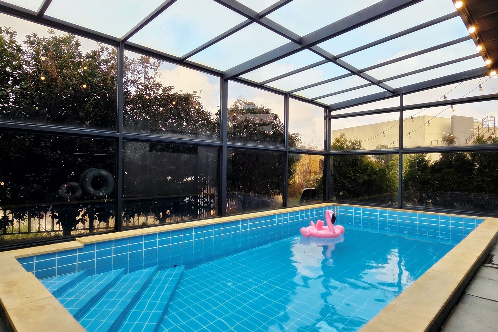 An indoor swimming pool with clear glass walls, a tiled floor, and a pink flamingo float.