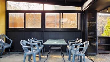 Un área de estar al aire libre con una mesa, sillas, ventanas grandes y vistas al exterior.