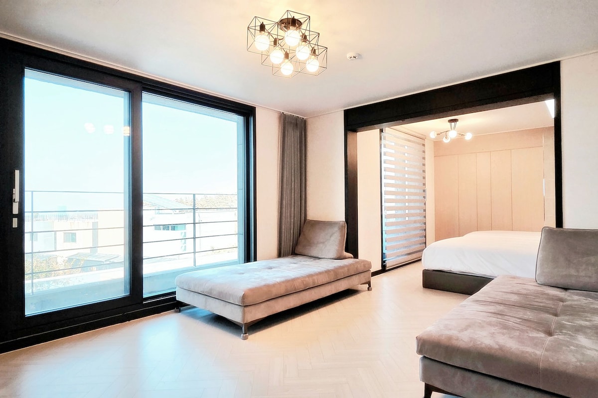 A modern bedroom with a sofa, a bed, and a large window.