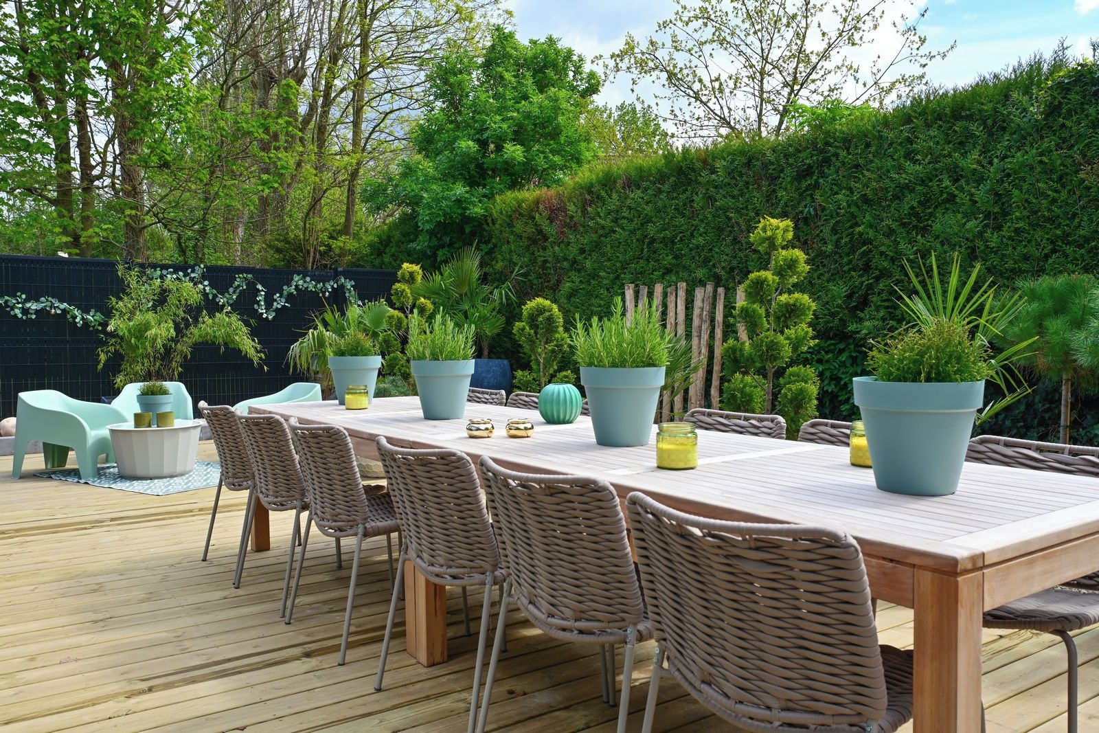 A wooden deck with a table and chairs, surrounded by greenery and a fence.