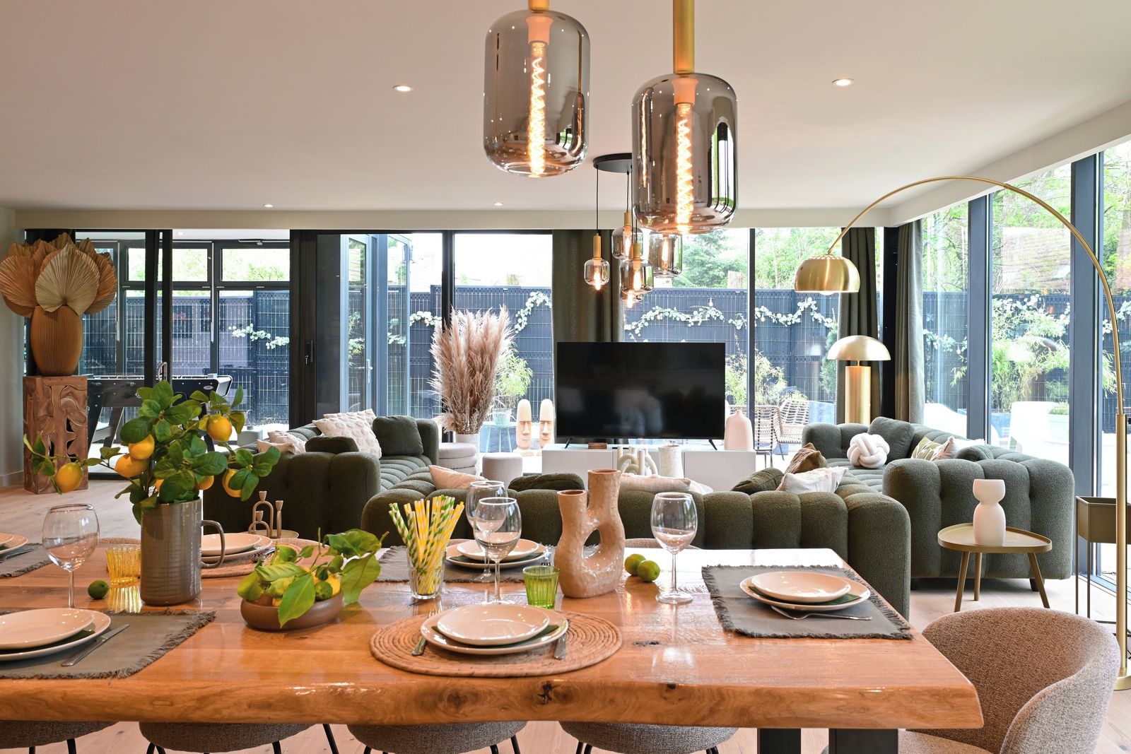 A modern living room with a dining area, large windows, and a flat-screen TV.