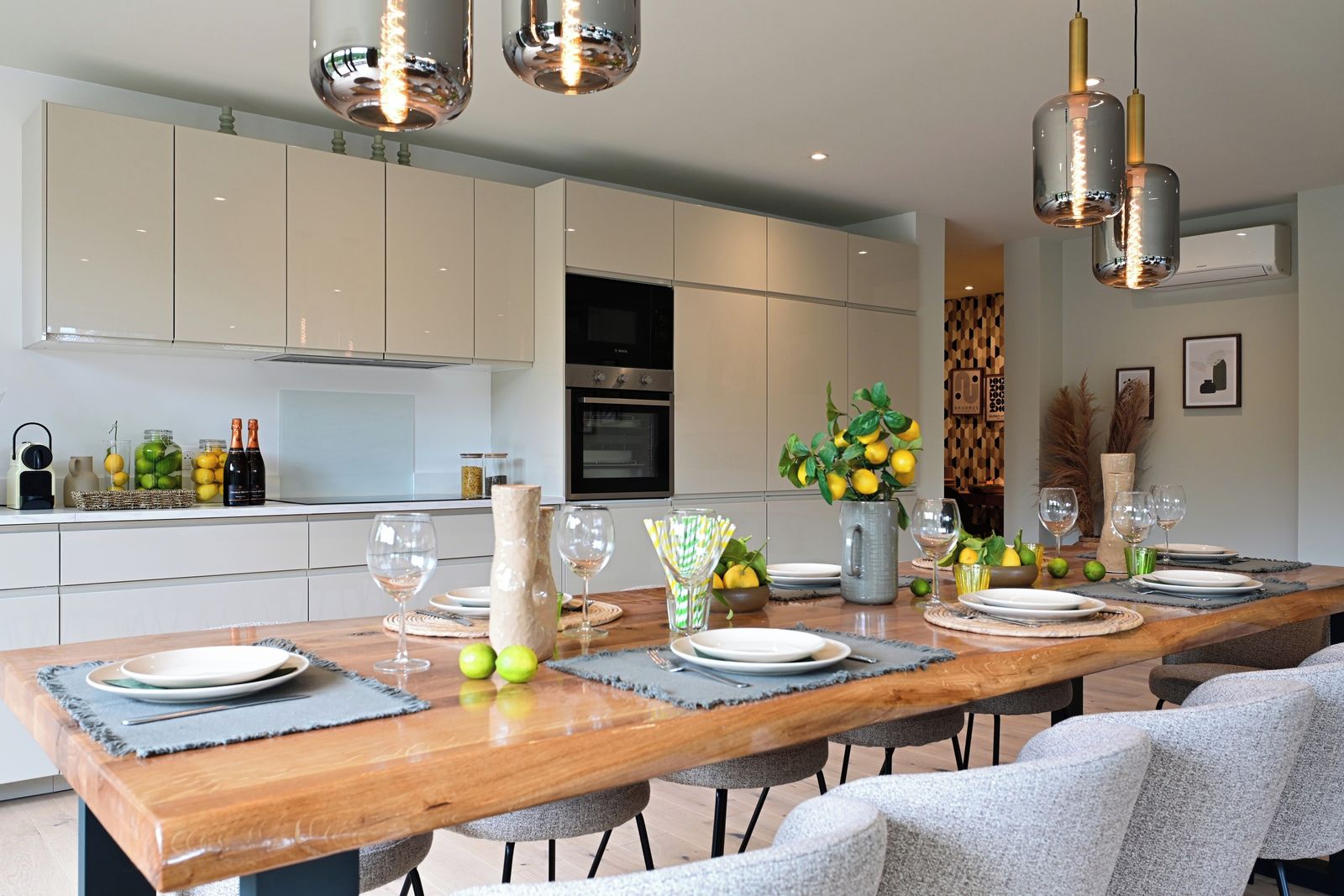 A modern kitchen with a wooden dining table set for six, equipped with a built-in oven, and a dining area with a view of the kitchen.