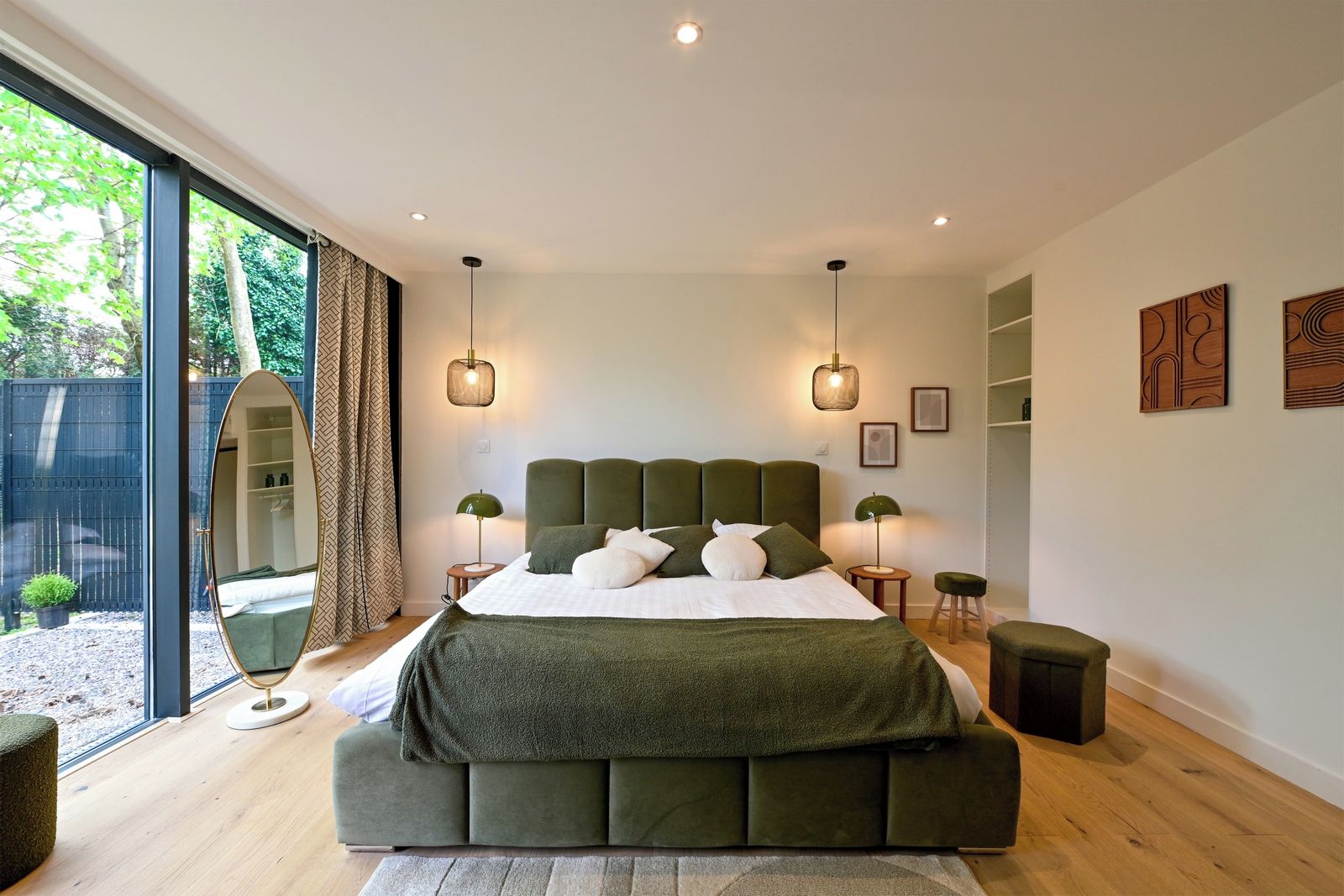 A modern bedroom with a large bed, two bedside tables, a mirror, and a view of the outdoors.