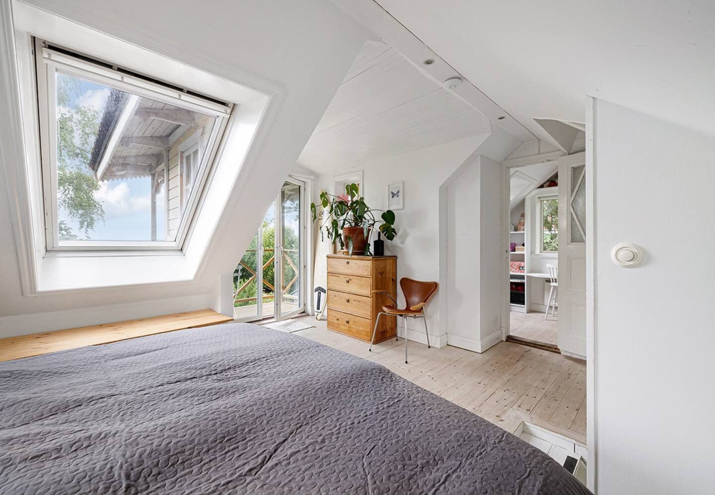A bedroom with a sloped ceiling, a large window, a bed, a dresser, and a chair.