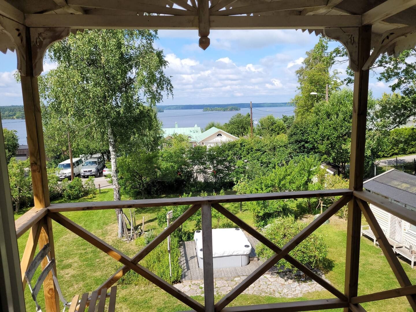 A gazebo with a view of a lake, trees, and a building with a green roof.