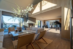 A spacious living area with a large window, a piano, and a view of a bridge. - Exclusive Beachfront Villa (Saltsjo-Duvnas)