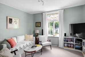 Ein Wohnzimmer mit Sofa, Sessel, Couchtisch und Bücherregal.