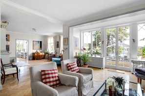 A spacious living room with a large window, a dining area, and a cozy seating area with armchairs and a sofa. - Seaside Villa With Own Beach (Saltsjo-Duvnas)