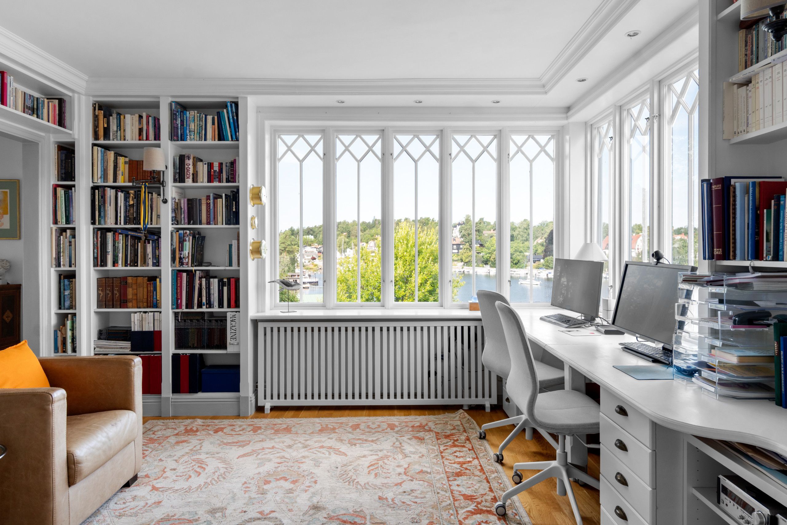A well-lit office space with a large window, a bookshelf, a desk with a computer, and a comfortable chair.