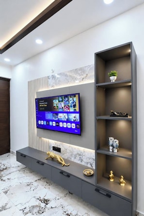 A modern entertainment unit with a flat-screen TV, built-in shelves, and decorative items. - Hidden Gem 4Bhk Villa in Greater Noida (Uttar Pradesh)